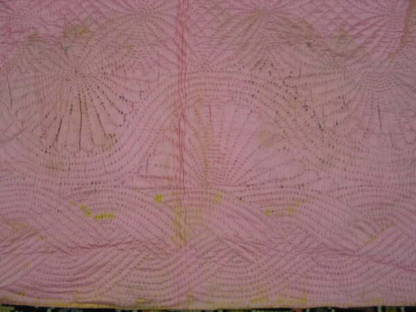 Pink quilted textile with dense dark stitching creating radiating fan and wave patterns.