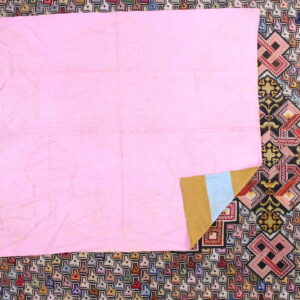 Multicolored low-pile rug with small repeating geometric patterns is mostly covered by a bright pink quilt.