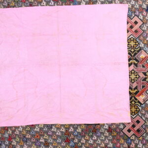 Pink quilted fabric covers a multicolored rug featuring dense geometric and cross-stitch patterns.