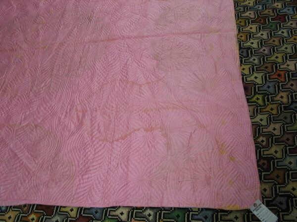 Quilted pink fabric with stains obscures a woven rug featuring a multi-colored, dark geometric pattern.