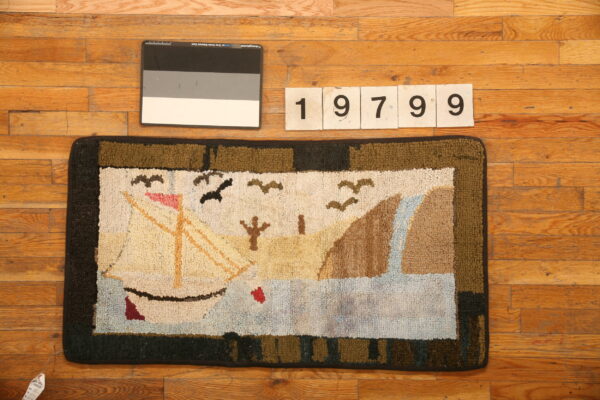 Hooked rug with a beige, blue, and green sailboat scene border sits on natural hardwood planks.
