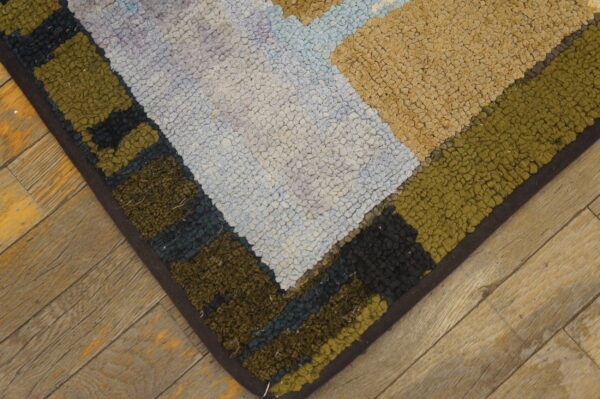 Chunky textured rug corner in beige, olive, light blue, and black geometric blocks rests on rustic wood flooring.