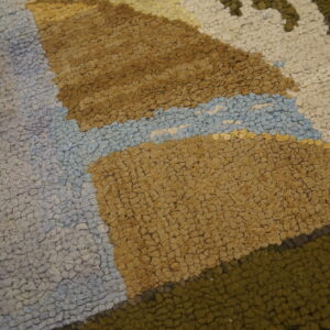 Textured rug pile featuring irregular color blocks in tan, light blue, cream, and olive green.