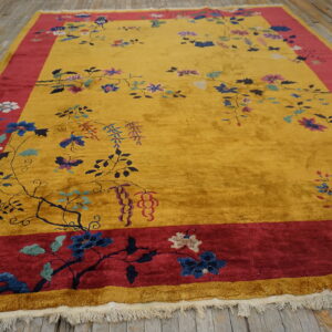 High-pile yellow rug with a wide red border and scrolling floral pattern lying on light wood planks.