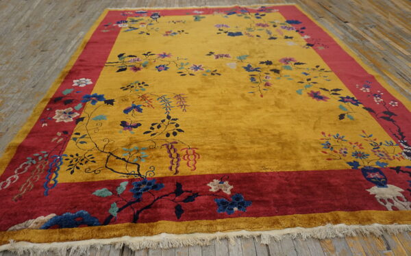 High-pile yellow rug with a wide red border and scrolling floral pattern lying on light wood planks.