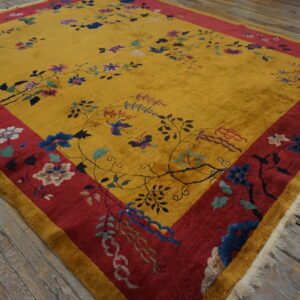 Gold and red high-pile rug with floral and vine patterns rests on distressed wooden floorboards.