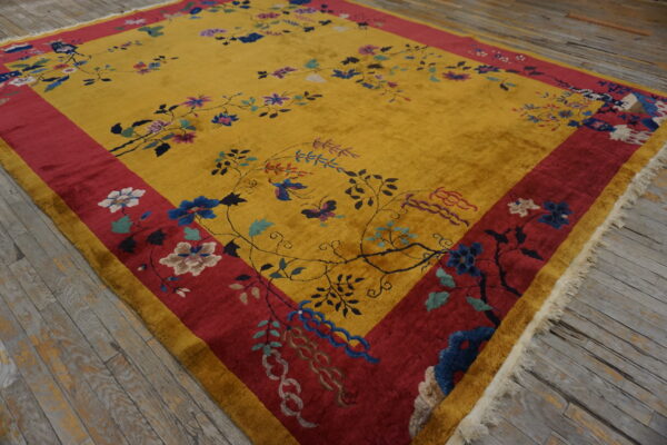 Gold and red high-pile rug with floral and vine patterns rests on distressed wooden floorboards.