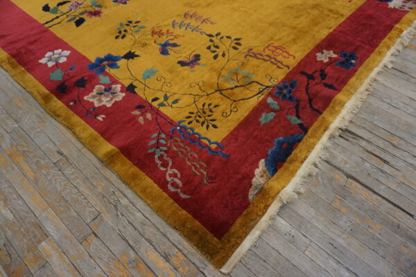 Plush yellow rug with a crimson border and intricate floral vine patterns rests on weathered gray wood flooring.