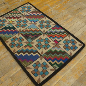 A colorful geometric rug with checkered diamonds and zigzag stripes rests on worn, light wood planks.