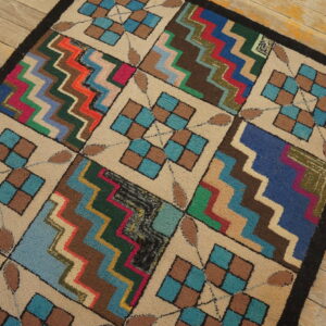 Multi-colored textured rug featuring checkerboard and zigzag blocks rests on rustic wooden planks.