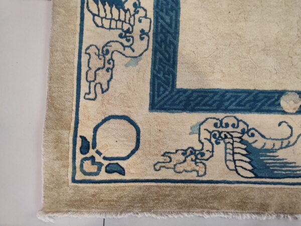 Tan and cream high-pile rug corner featuring blue traditional chinese patterns and geometric borders.