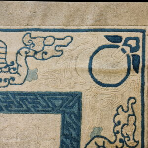 Beige rug detail with teal blue borders, stylized bird, cloud, and geometric corner patterns.
