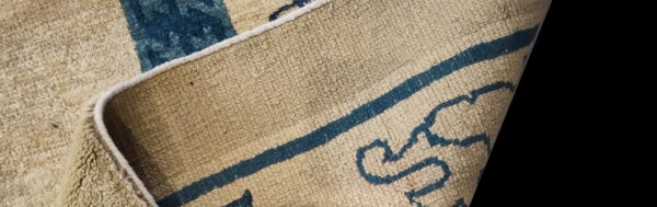 Textured beige rug with thick blue lines and abstract shapes is curled back showing the edge.