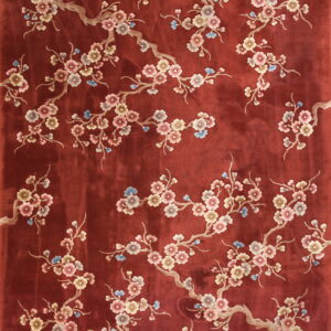Red low-pile rug with sprawling beige branches and pink, mauve, and blue blooming flowers.