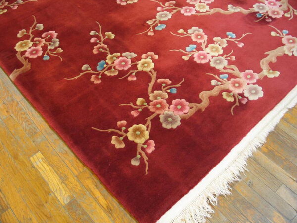 Close-up of a high-pile burgundy rug with floral branches and cream fringe on golden wood flooring.