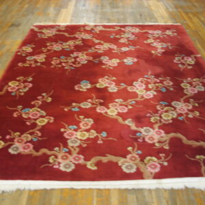 Deep red rug with pink, yellow, and blue floral branches lies on distressed yellow hardwood flooring.