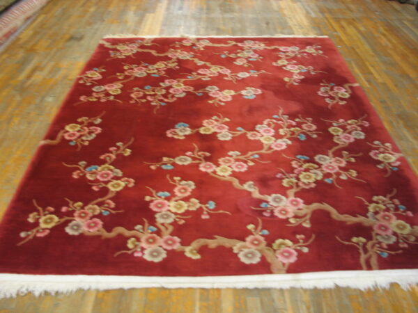 Deep red rug with pink, yellow, and blue floral branches lies on distressed yellow hardwood flooring.