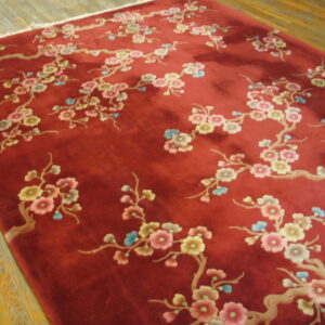 A high pile red rug with light pink, yellow, and blue flowering branches rests on light-colored wood planks.
