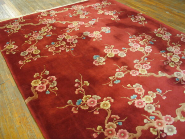 A high pile red rug with light pink, yellow, and blue flowering branches rests on light-colored wood planks.