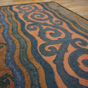 Low-pile rug featuring blue swirls and wavy stripes in rust, brown, and light blue on wood flooring.