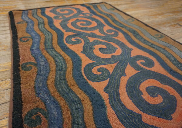 Low-pile rug featuring blue swirls and wavy stripes in rust, brown, and light blue on wood flooring.