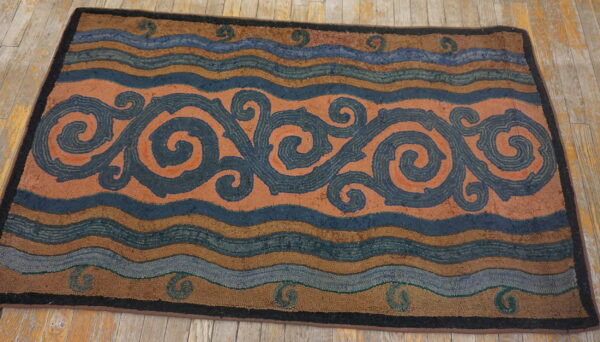 Rust, blue, and brown hooked rug with scrolling vines and wavy stripes rests on distressed wood planks.