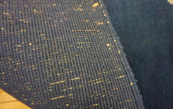 Close-up of a dark blue ribbed rug with tan speckles resting on a light wooden surface.