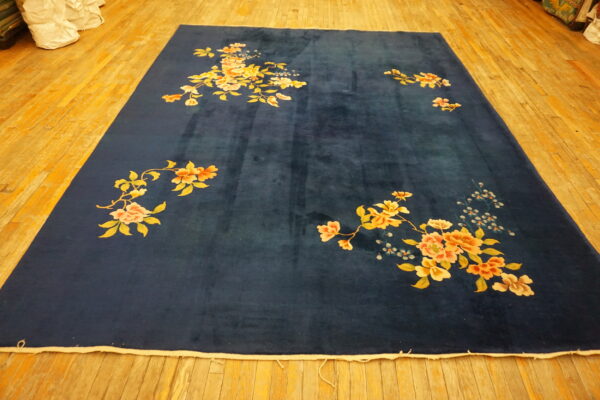 Large deep blue rug with scattered peach, yellow, and cream floral patterns on wooden floorboards.