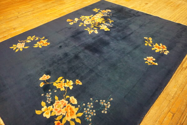 Deep blue high-pile rug featuring large scattered yellow and peach florals rests on golden hardwood flooring.