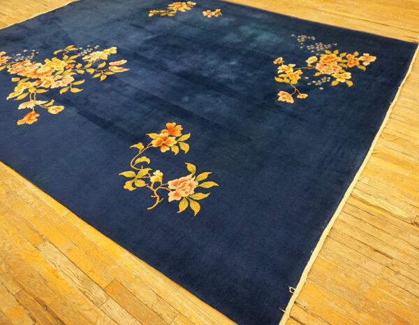 Velvety indigo rug featuring scattered peach and yellow blossoms rests on a distressed wood floor.
