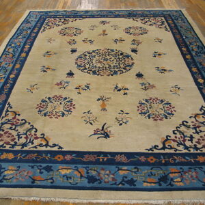 Large rectangular beige rug featuring intricate blue borders and scattered multicolor floral medallions on a wood floor.