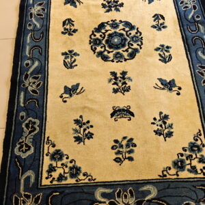 Cream rug with medium pile and navy blue floral patterns, bordered in blue, displayed on light tile.