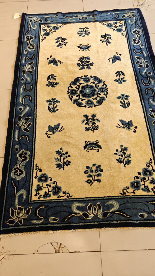 Cream rug with medium pile and navy blue floral patterns, bordered in blue, displayed on light tile.