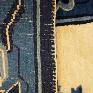 Dark blue patterned rug is folded over, exposing the light beige textured reverse side.