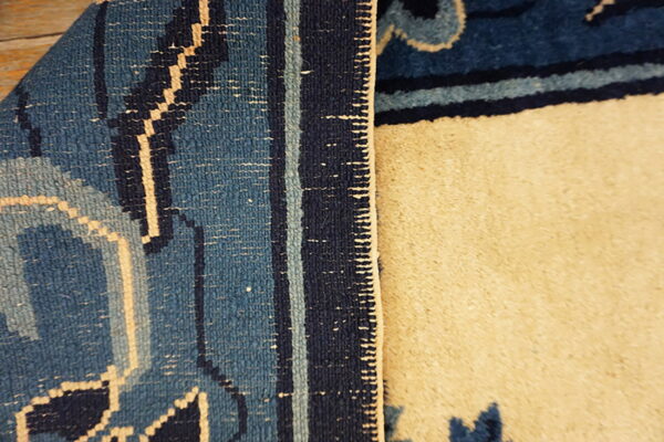 Dark blue patterned rug is folded over, exposing the light beige textured reverse side.