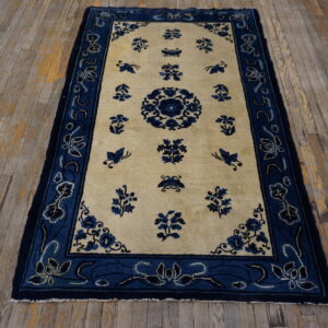 Blue floral pattern on a cream field rug with a wide blue border, laid over distressed wooden floorboards.