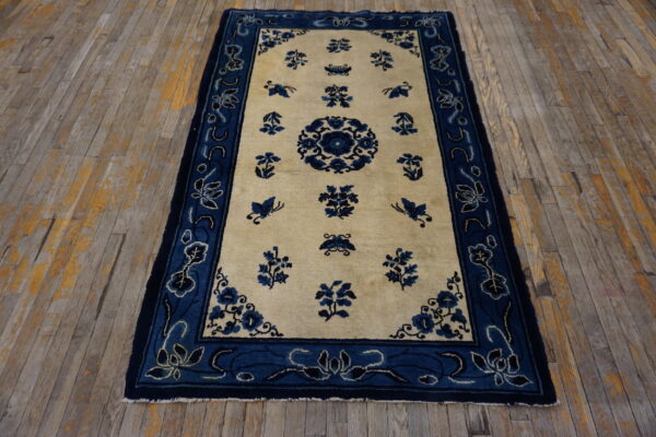 Blue floral pattern on a cream field rug with a wide blue border, laid over distressed wooden floorboards.