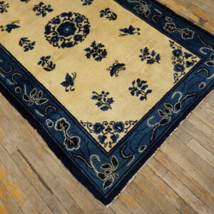 Cream and indigo rug featuring a floral pattern and wide border, placed on worn wood flooring.