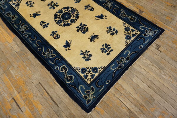 Cream and indigo rug featuring a floral pattern and wide border, placed on worn wood flooring.