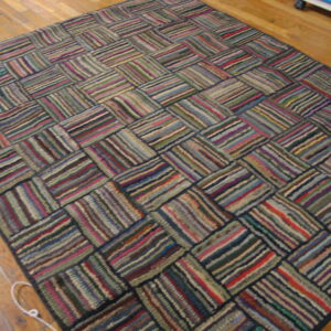 Highly textured, multicolored rug with a geometric striped block design on wood planks.