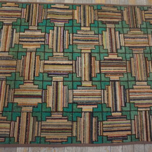 A heavily textured rug featuring a multicolored geometric pattern of stripes and green crosses on distressed wood flooring.