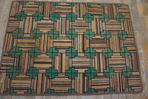 A heavily textured rug featuring a multicolored geometric pattern of stripes and green crosses on distressed wood flooring.