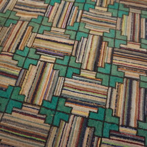 Close-up of a textured rug featuring a teal geometric lattice framing multicolored, striped rectangular sections.