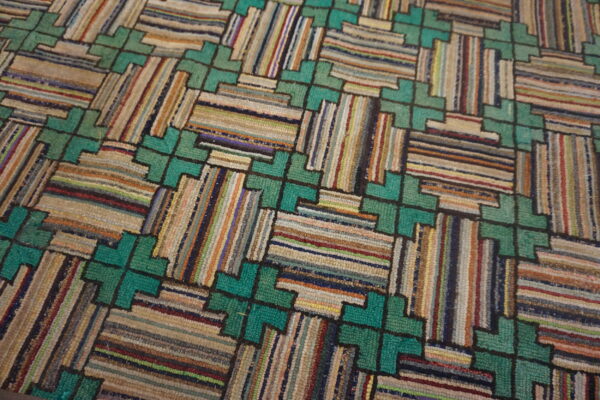 Close-up of a textured rug featuring a teal geometric lattice framing multicolored, striped rectangular sections.
