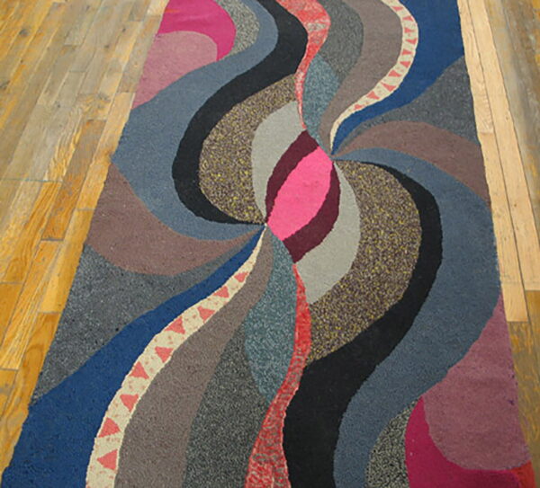 Abstract runner rug with swirling bands of pink, blue, gray, and brown colors on light plank flooring.