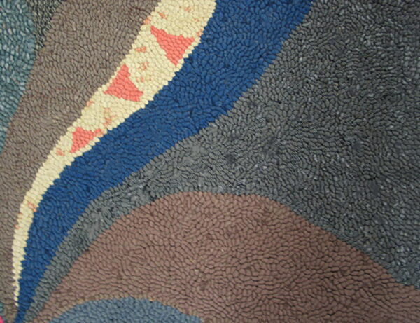 Textured rug showing curved bands of grey, blue, and brown, with a cream stripe featuring pink triangle motifs.