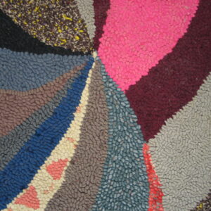 A heavily textured rug displays a multicolored radial pattern using broad sections of pink, blue, and gray.