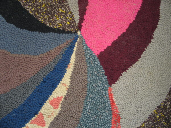 A heavily textured rug displays a multicolored radial pattern using broad sections of pink, blue, and gray.