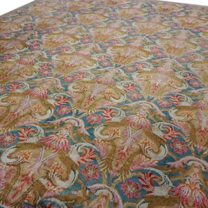 Ornate area rug with teal, rose, tan, and cream foliate motifs and a solid beige border.