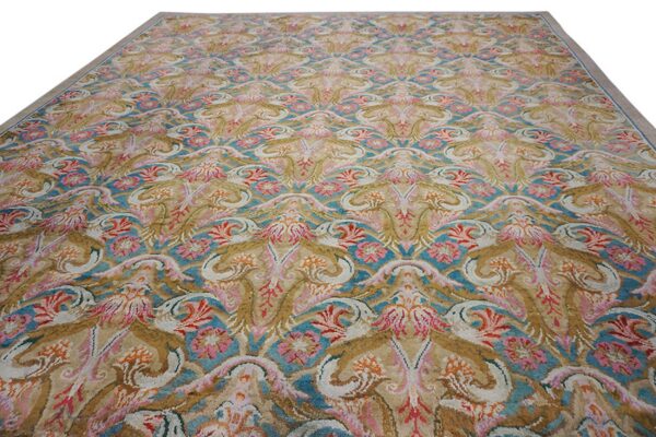 Ornate traditional rug with repeating floral medallions in gold, turquoise, pink, and white.
